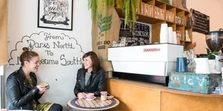 Two women holding coffee laughing in cafe spot width 968